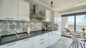 Una cocina moderna con armarios blancos, un salpicadero con diseño y vistas al mar a través de amplios ventanales.