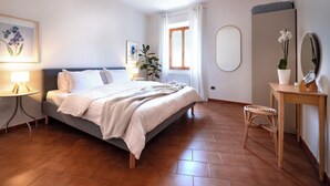 Een slaapkamer met een bed, nachtkastje, lamp, potplant en een spiegel.