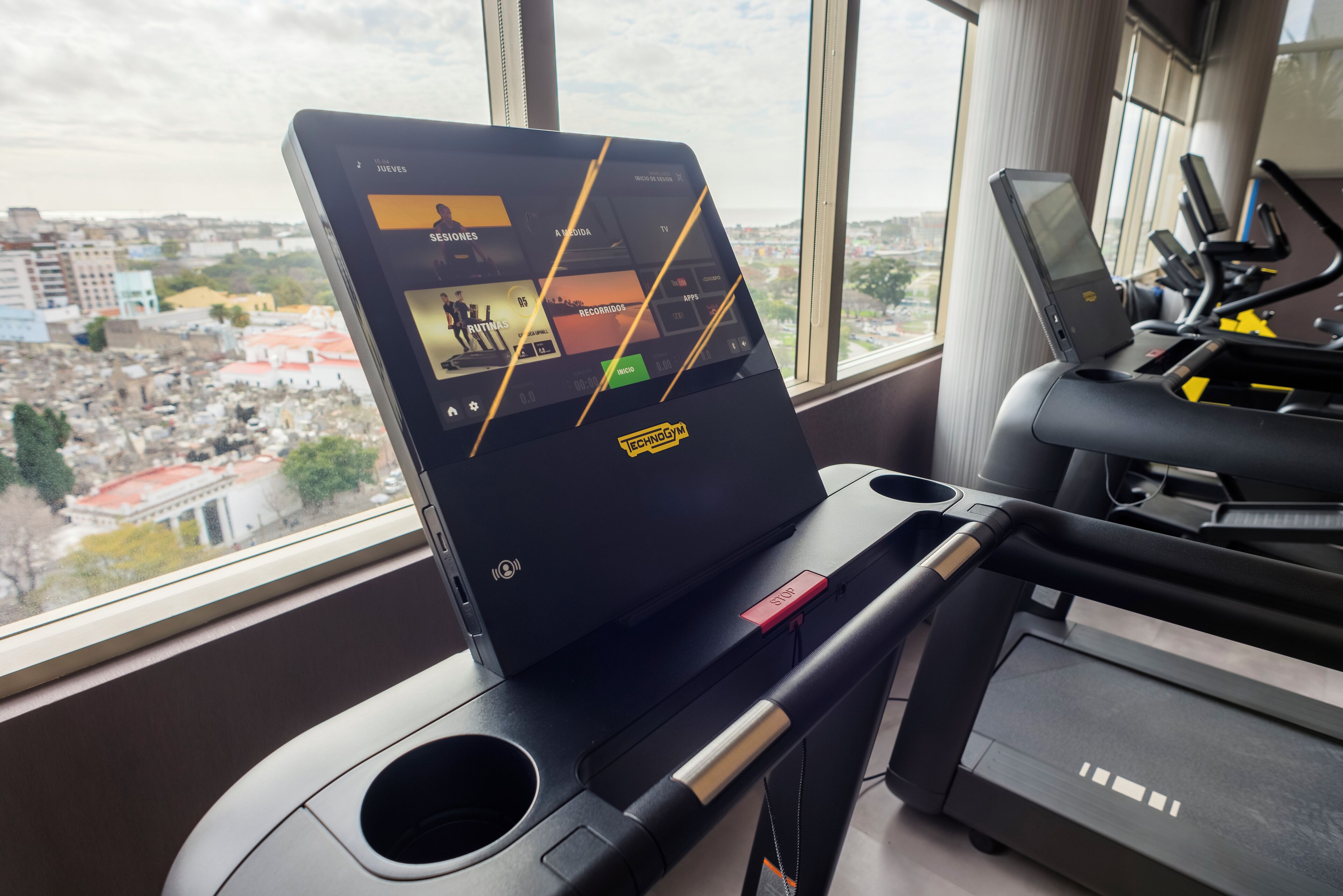 Ein Laufband mit digitalem Display und Blick auf die Stadt durch große Fenster.