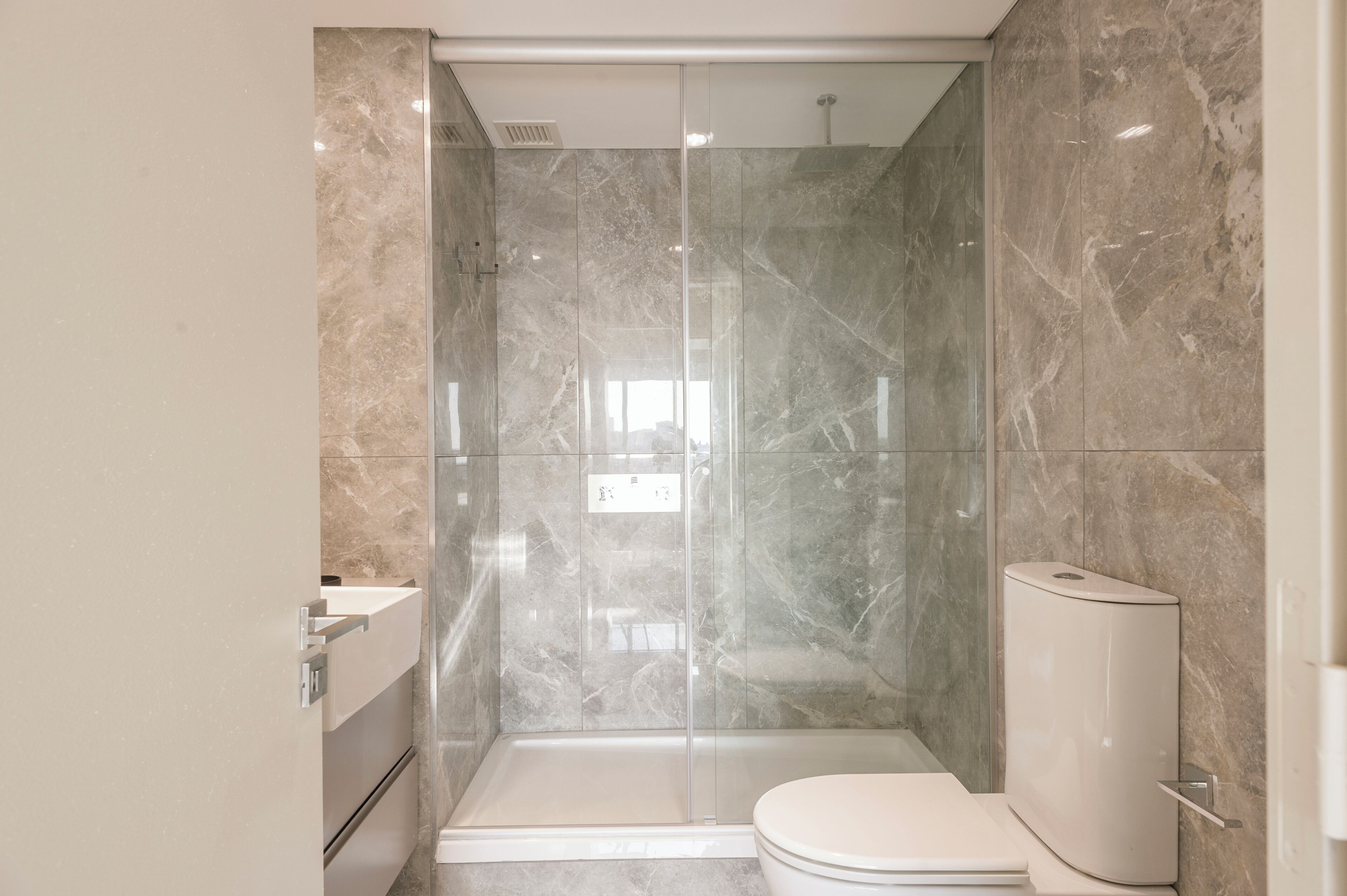 A modern bathroom with a glass-enclosed shower, a toilet, and a sink.