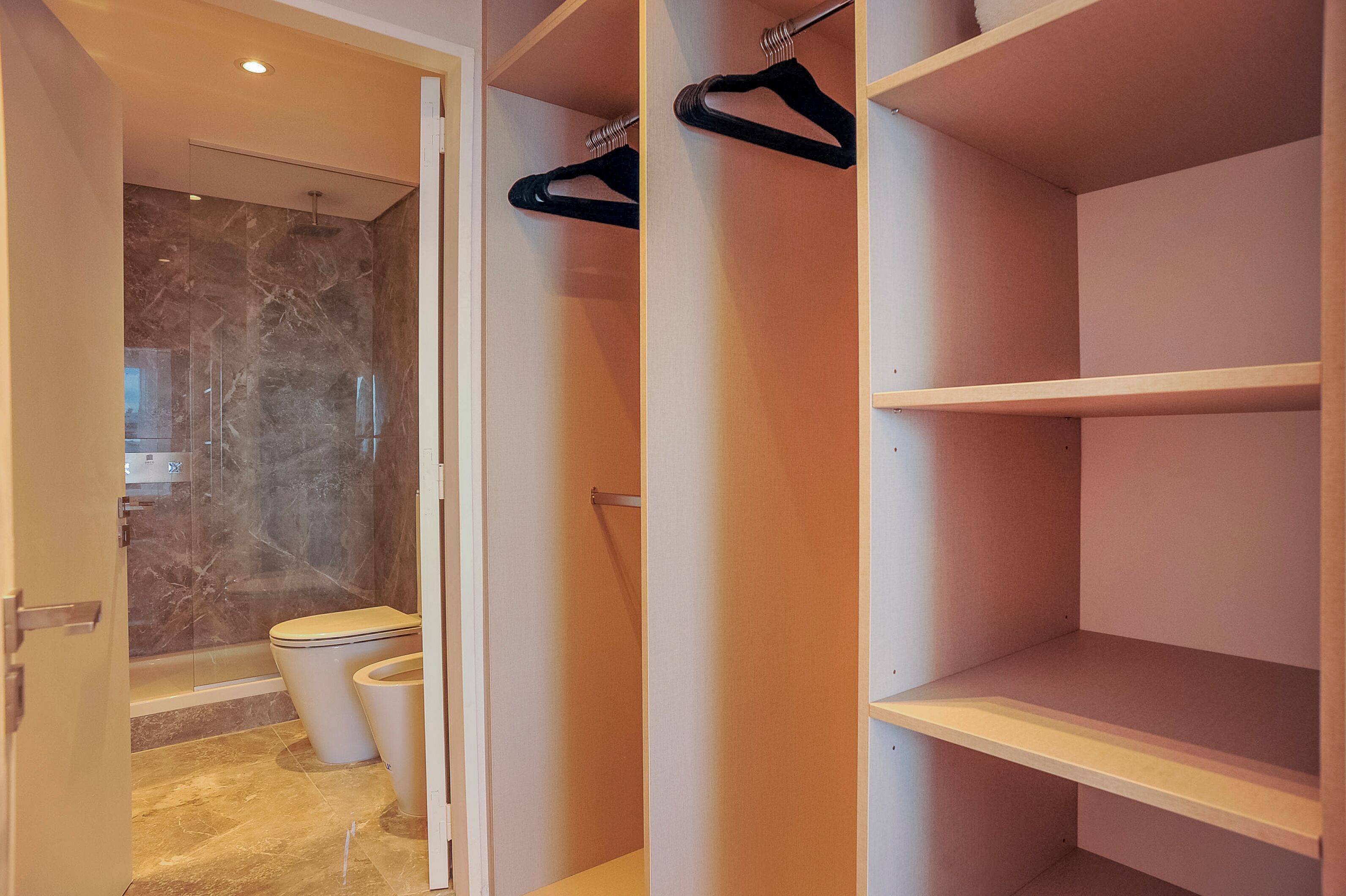A bathroom with a shower, two toilets, and a walk-in closet with shelves and hangers.