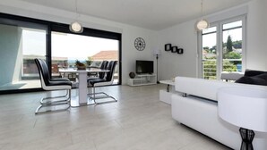 A modern living room with a dining area, large windows, and a flat-screen TV. - Vlads' Place - pool & garden-view (Slatine)