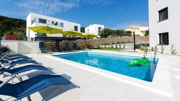 A swimming pool with sun loungers and umbrellas, surrounded by modern buildings. - Vlads' Place - pool & garden-view (Slatine)