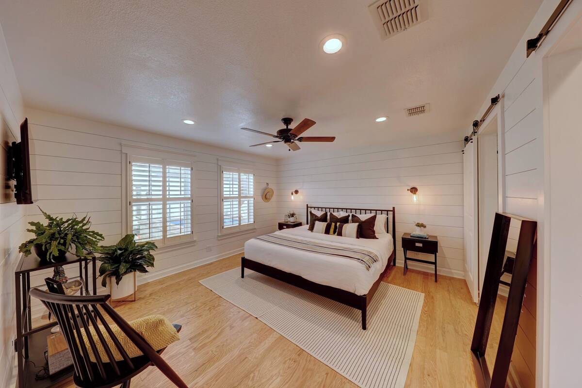 Un dormitorio con cama, ventilador de techo, mesita de noche, espejo y una escalera.