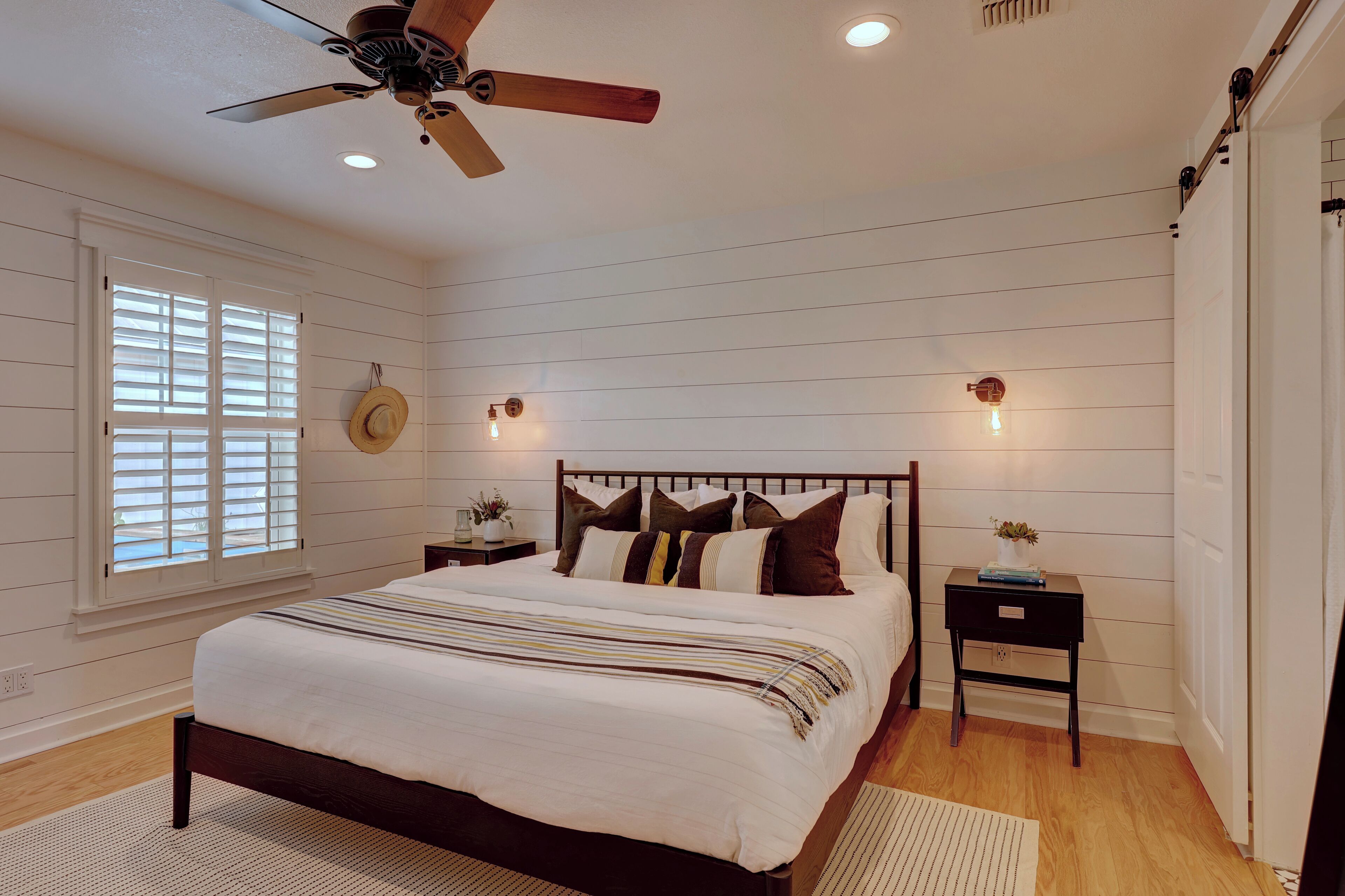 A bedroom with a bed, a ceiling fan, a nightstand, and a window with blinds.