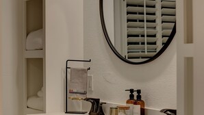 Un baño con tocador blanco, mueble de madera oscura y un espejo redondo.
