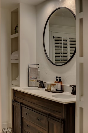 A bathroom with a white vanity, dark wooden cabinet, and a round mirror. - Wanderers Retreat House (Comfort)