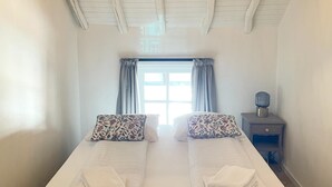 A double bed with floral-patterned pillows and folded towels, a nightstand with a lamp, and a window with curtains. - Voerendaal Family Apartment (Voerendaal)