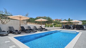 A swimming pool with lounge chairs and umbrellas, surrounded by a tiled deck.
