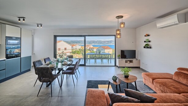 A modern living room with a large window, a dining area, and a kitchen.