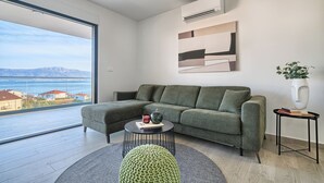 A modern living room with a green sofa, a round coffee table, and a view of the sea through large windows. - Imola‘s Place - Sea-View & Pool (Slatine)