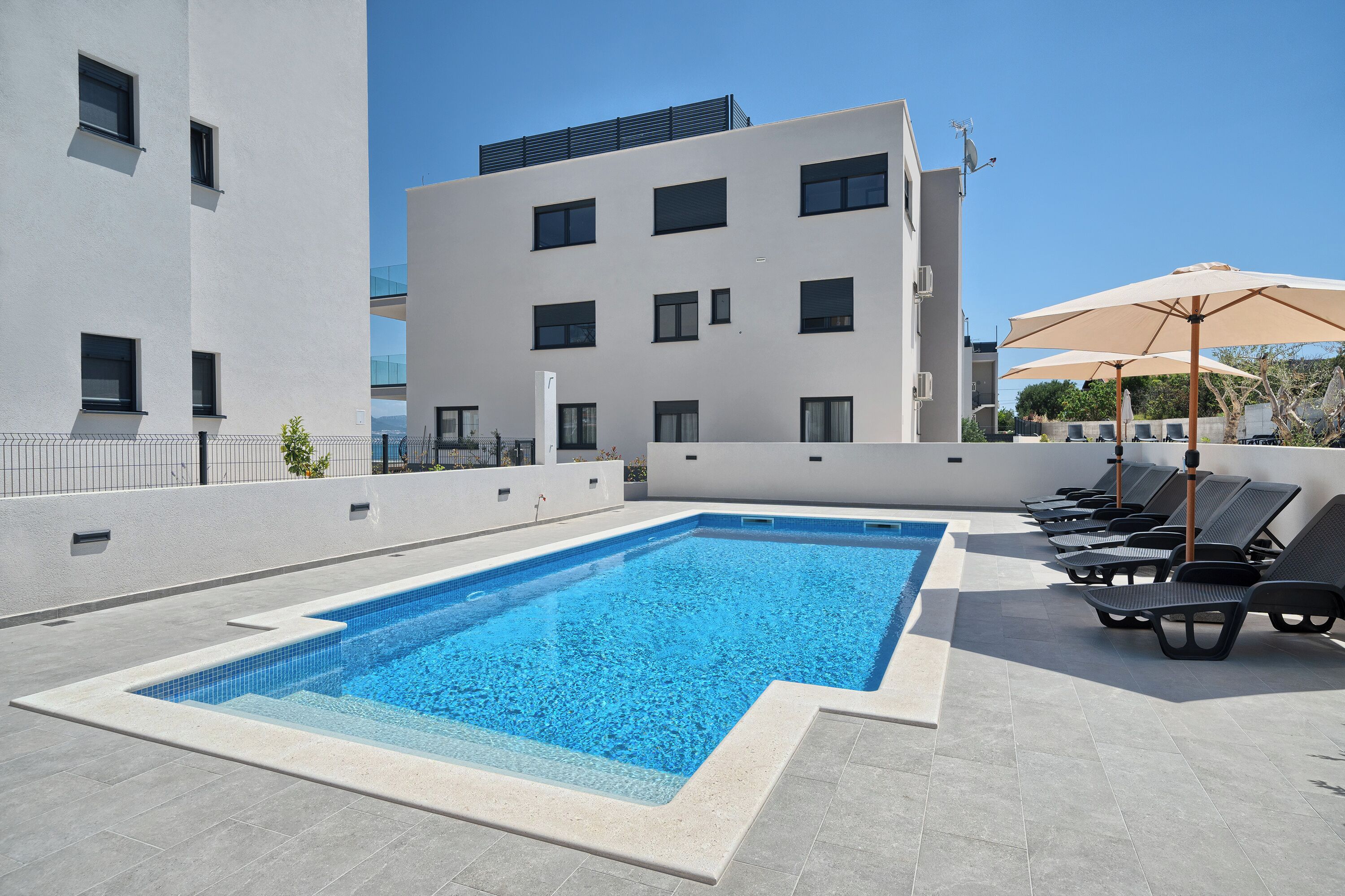 A rooftop swimming pool with lounge chairs and umbrellas, surrounded by modern buildings.