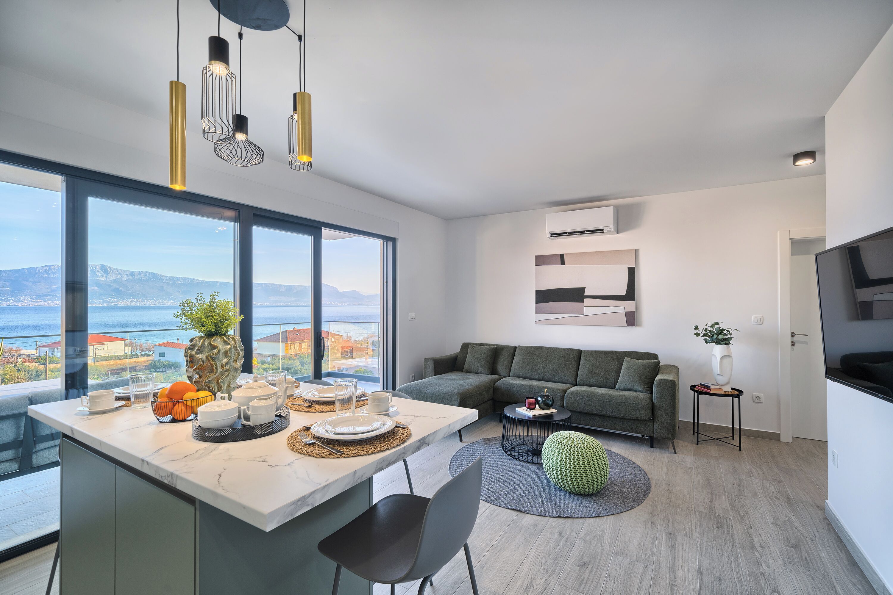 A modern living room with a dining area, large windows with a view, and a flat-screen TV.
