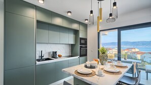 A modern kitchen with green cabinets, a marble countertop, and a dining area with a table set for two. - Imola‘s Place - Sea-View & Pool (Slatine)