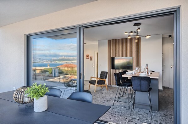 Un espace repas moderne, doté d’une grande table, de chaises et offrant une vue à travers une porte vitrée.