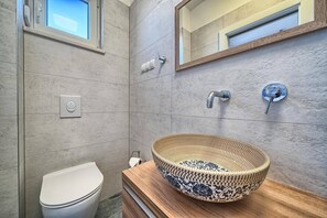 Ein modernes Badezimmer mit einem großen, gewebten Waschtischbecken, einer Toilette und einem Spiegel über dem Waschbecken.