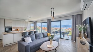 A modern living room with a grey sofa, a round coffee table, and a view of the city through large windows. - Aqualis Vista (Slatine)