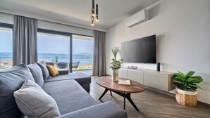 A modern living room with a grey sofa, a wooden coffee table, and a large TV on the wall. - Aqualis Vista (Slatine)