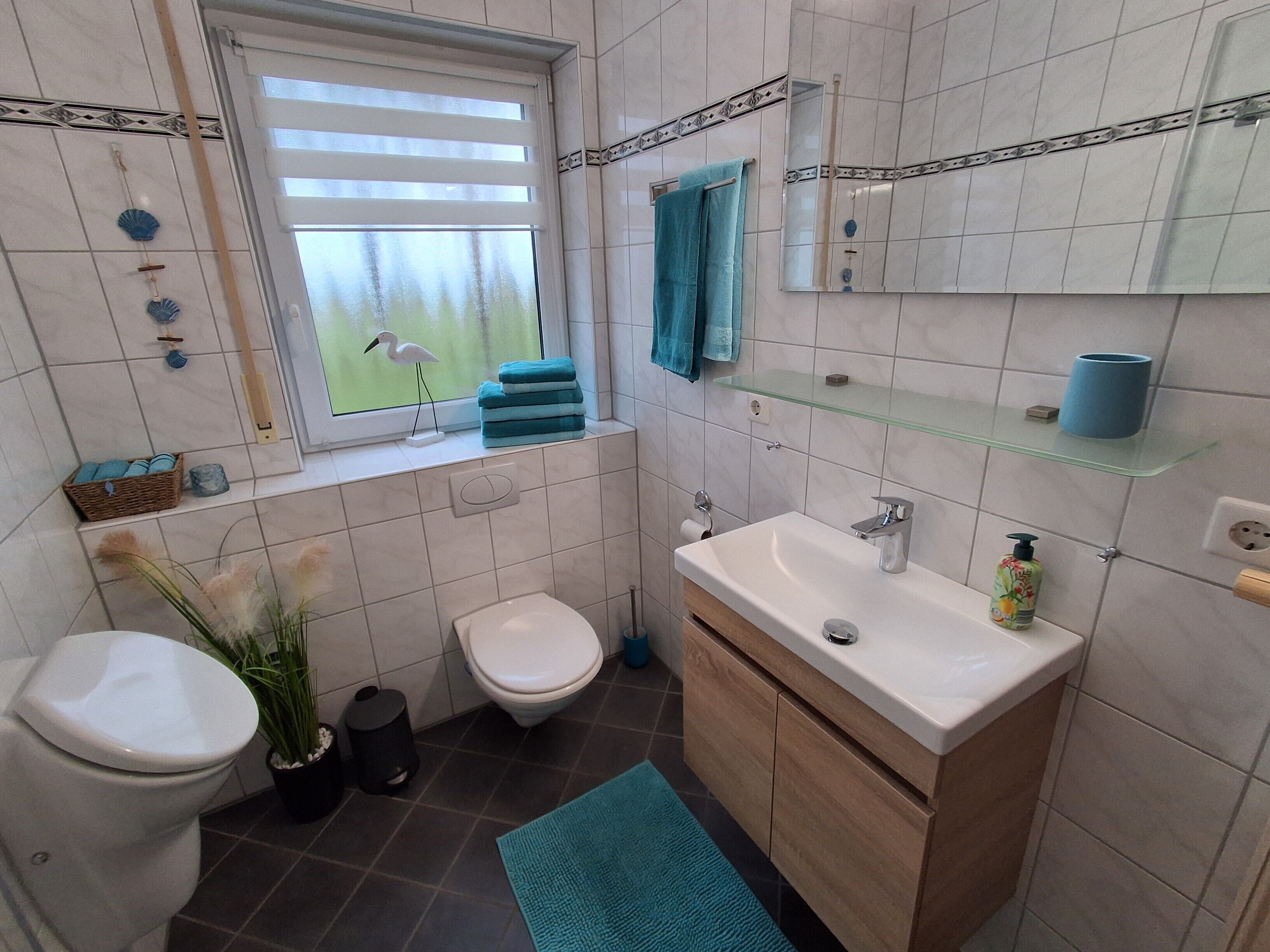 A bathroom with a toilet, bidet, sink, and a window with a view of trees.