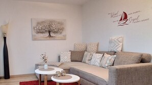 A modern living room with a grey sofa, two white side tables, a red rug, and a wall art piece. - Apartment 'Lounge' with Mountain View, Private Terrace and Wi-Fi (Sigmarszell)