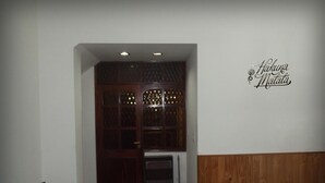 Ein Zimmer mit einer dunklen Holztür, einer weißen Wand mit einem dekorativen Schild und einem schwarzen Sofa mit einem farbenfrohen Kissen.