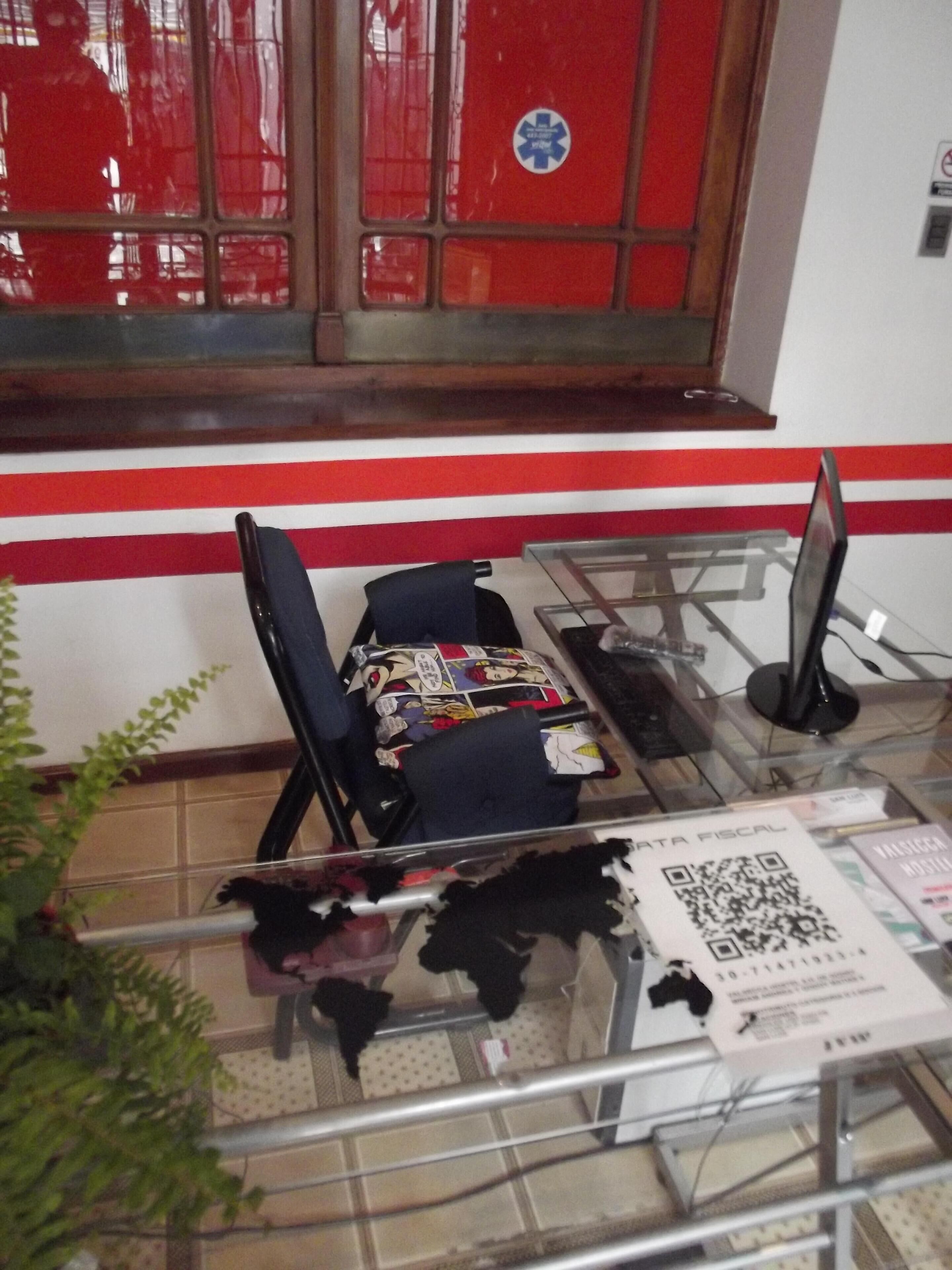 A room with a glass table, a black chair, a red and white striped wall, and a window with a red curtain.