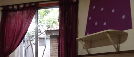 Una habitación con una cama, una ventana con cortinas rojas y una pared morada con estampado floral.