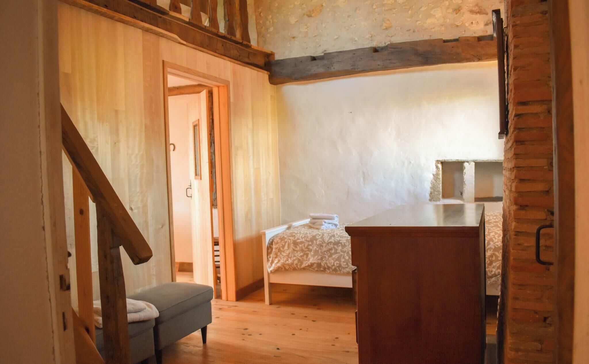 A bedroom with a bed, a wooden dresser, a bench, and a door leading to another room.