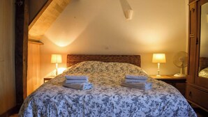 A bedroom with a wooden headboard, two bedside lamps, a bed with floral bedding, and a fan on the nightstand. - Saint Privat House: Pool, Family & Greenery (Saint Privat en Périgord)