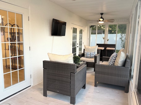 A covered patio area with wicker furniture, a flat-screen TV mounted on the wall, and a ceiling fan.