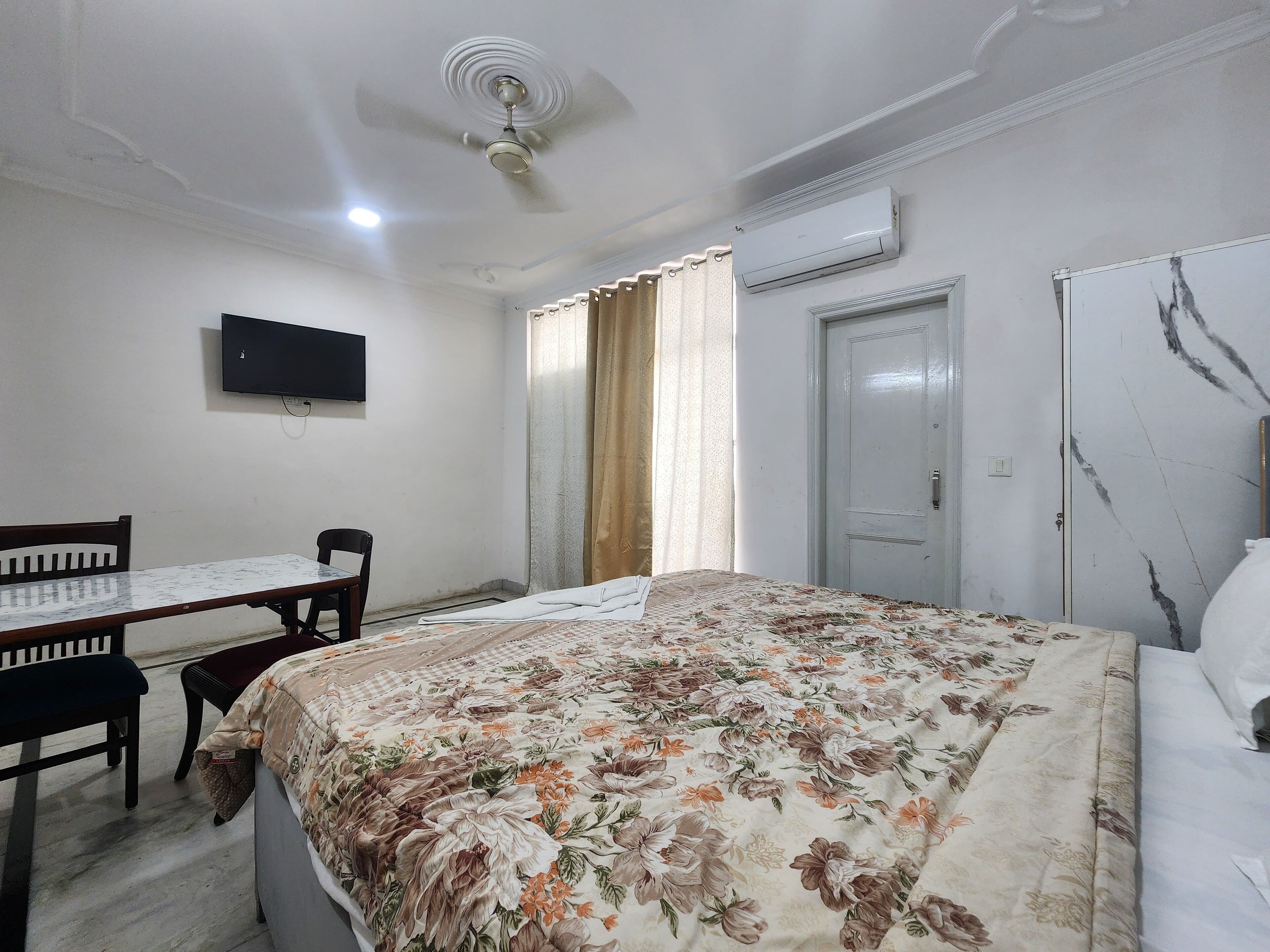 Une chambre à coucher comprenant un lit, un bureau, une chaise, un téléviseur, un appareil de climatisation et une porte.