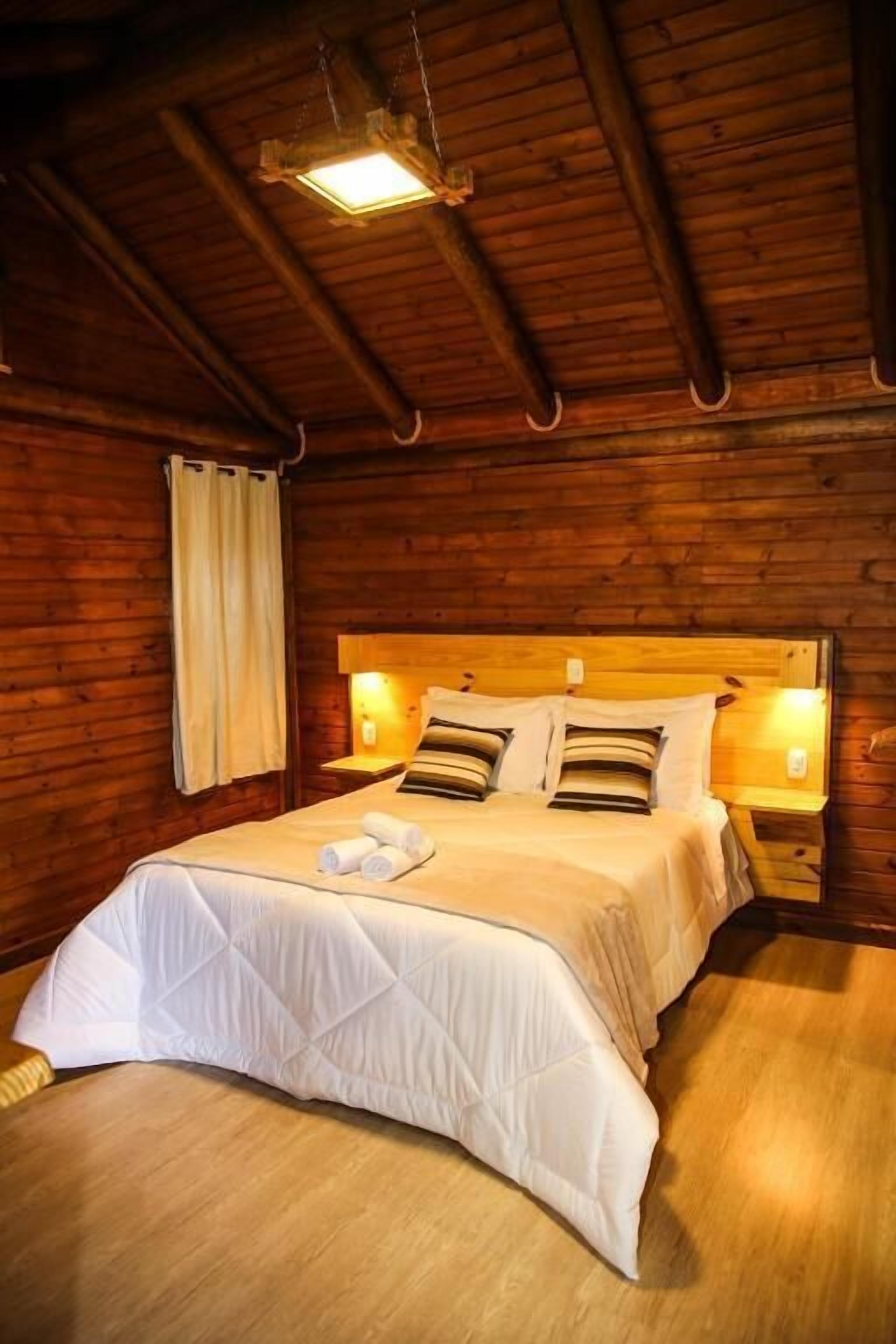Una habitación tipo cabaña de madera con una cama, dos lámparas de noche y una lámpara colgante.