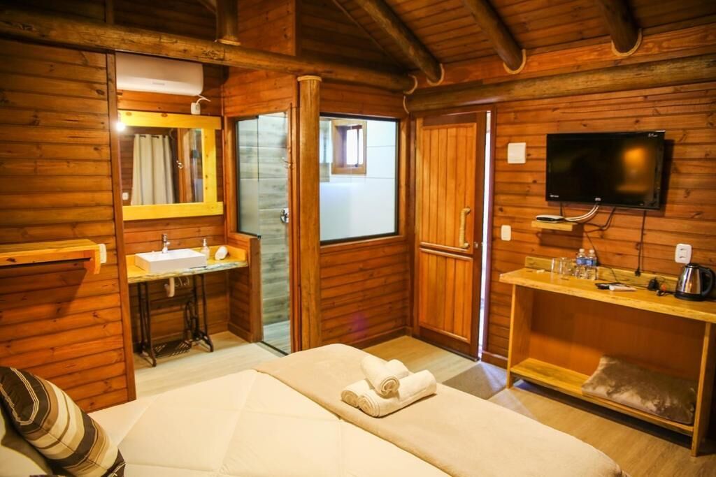 A wooden cabin room with a bed, a sink, a mirror, a television, and a small table with a kettle.