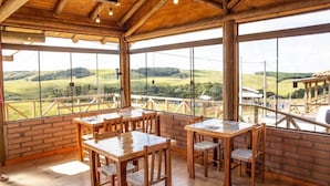 A spacious indoor area with large windows offering a view of rolling hills. There are wooden tables and chairs arranged for dining. - Pousada Morada da Serra (Cambara do Sul)