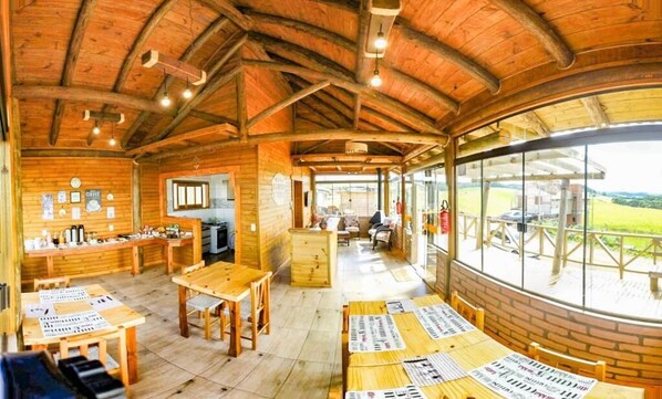 A rustic wooden interior with a dining area, kitchen, and large windows offering a view of the outdoors. - Pousada Morada da Serra (Cambara do Sul)