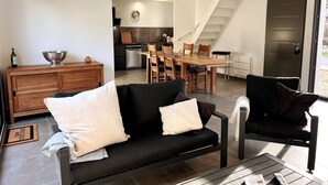 A modern living room with a sofa, a dining table, and a kitchen in the background. - Spacious House in Libourne – Near Saint-Émilion and Bordeaux (Libourne)