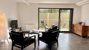 A modern living room with a dining table, two black sofas, a TV, and a sliding glass door leading to an outdoor area. - Spacious House in Libourne – Near Saint-Émilion and Bordeaux (Libourne)