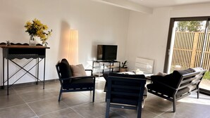 A modern living room with a sofa, two armchairs, a TV, a lamp, and a small table with a vase of flowers. - Spacious House in Libourne – Near Saint-Émilion and Bordeaux (Libourne)