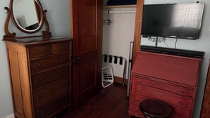 Una habitación con un aparador de madera, un espejo, un tocador rojo, un televisor y un armario con perchero.