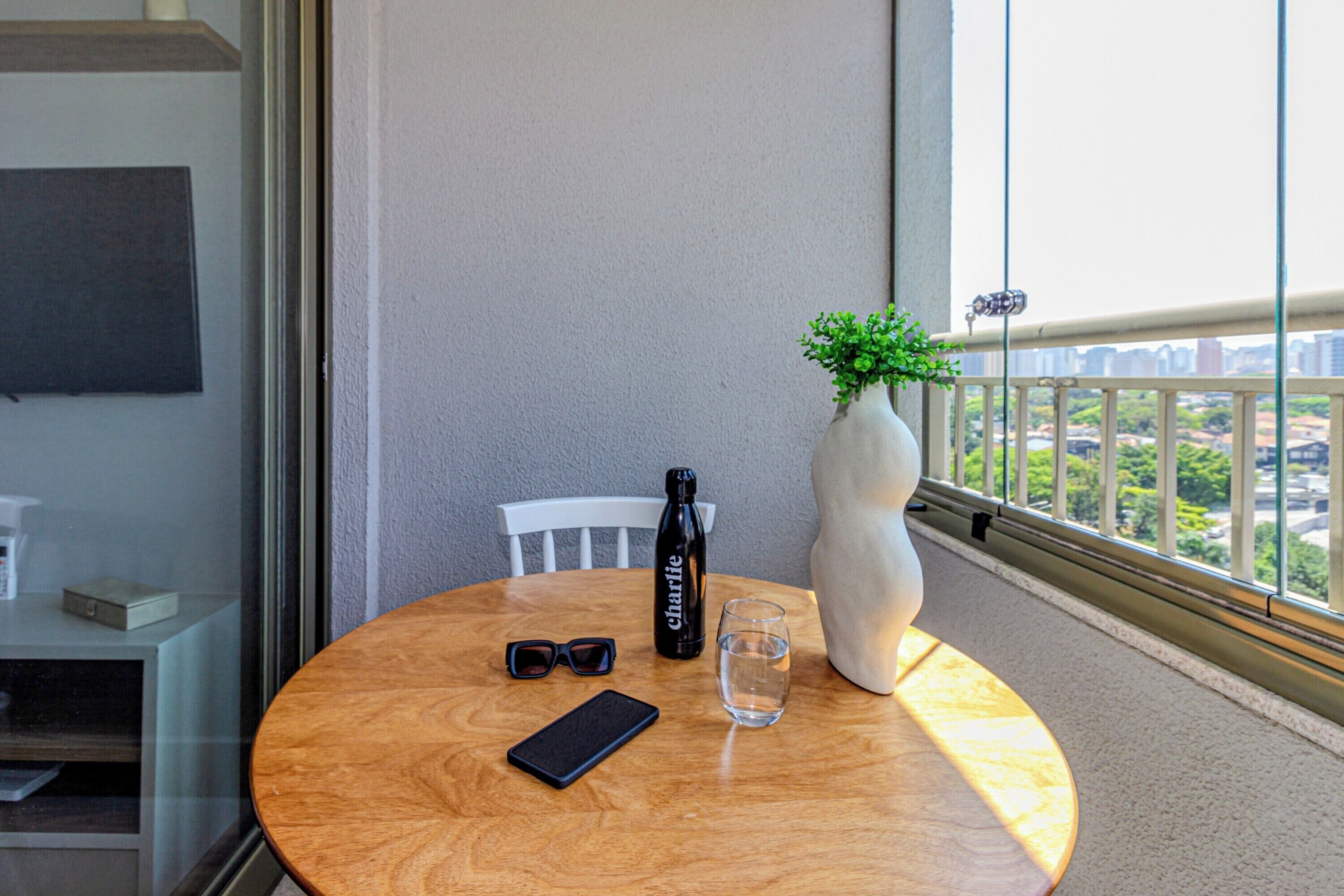 Una mesa redonda de madera con una botella, un vaso y un teléfono inteligente.