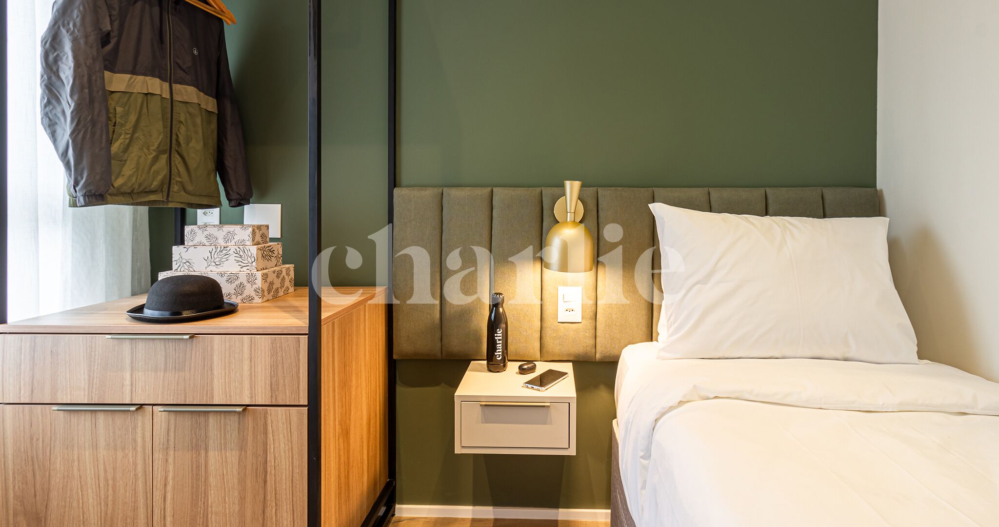 Une chambre d’hôtel bien rangée, avec un lit, une table de chevet et un manteau accroché au mur.