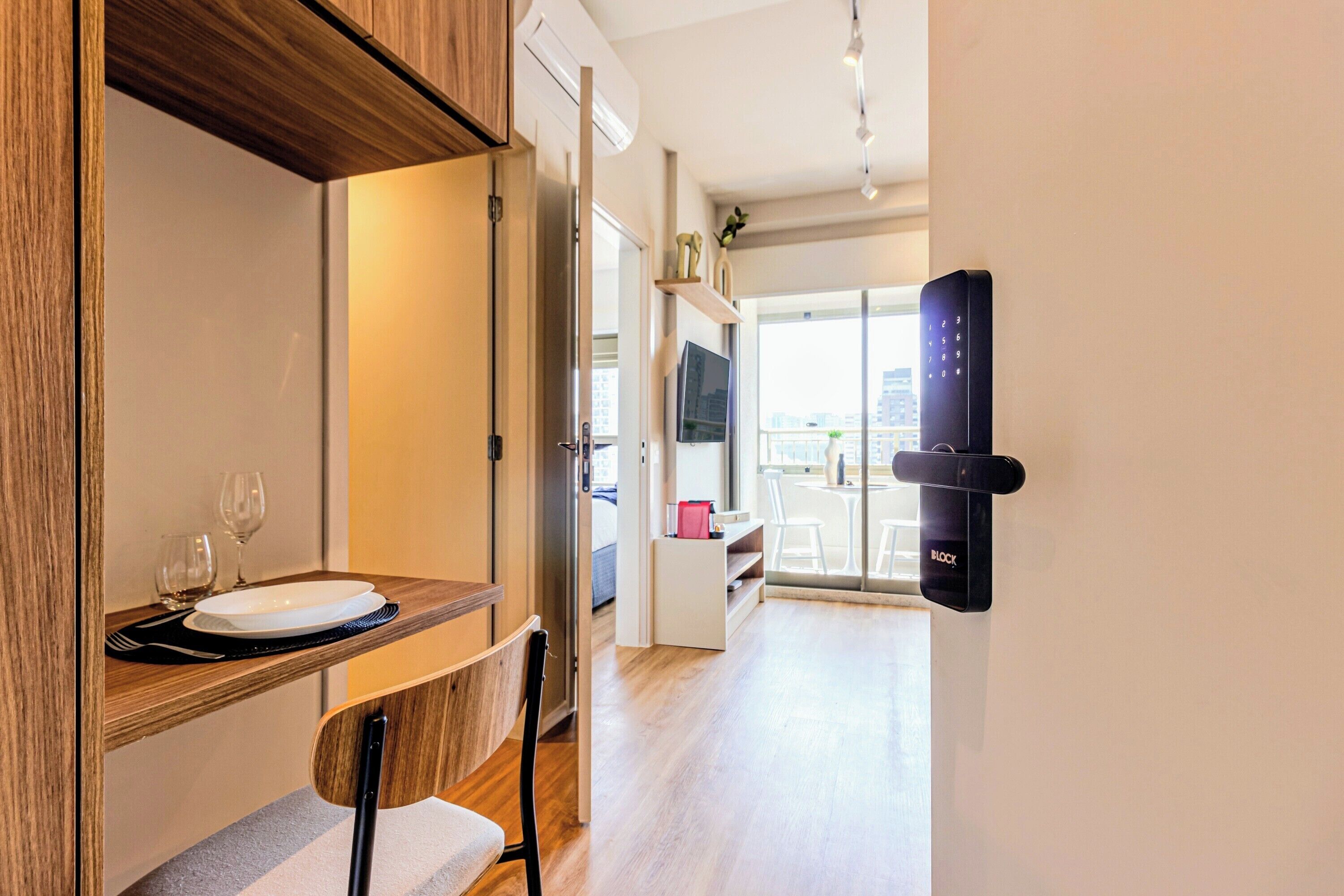 A modern hotel room with a dining area, a flat-screen TV, and a digital lock on the door.