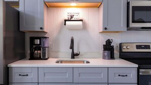 Une cuisine avec des meubles de couleur grise, un évier en acier inoxydable, une machine à café, un four à micro-ondes et un grille-pain.