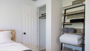 Une chambre avec un lit, une porte blanche et une étagère intégrée où sont rangées des serviettes et des oreillers pliés.