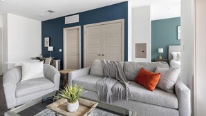 A living room with a grey sofa, a coffee table with a plant, and a blue accent wall. - Landing | Incredible 1BD, Pool, Gym (McKinney)