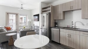 A modern kitchen with a built-in refrigerator, a dining table, and a sofa in the adjacent living area. - Landing | Incredible 1BD, Pool, Gym (McKinney)
