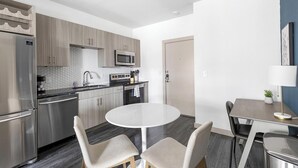 A modern kitchen with stainless steel appliances, a round dining table, and two chairs. - Landing | Incredible 1BD, Pool, Gym (McKinney)