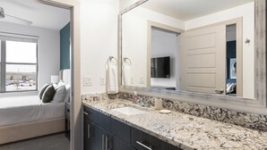 A hotel room with a bed, a bathroom with a sink and mirror, and a view of a parking lot. - Landing | Stylish 1BD, Gym, Pool (McKinney)