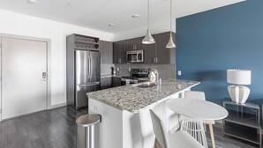 A modern kitchen with stainless steel appliances, a marble island, and bar stools. - Landing | Stylish 1BD, Gym, Pool (McKinney)