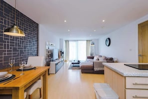 A modern apartment with a dining area, living room, kitchenette, and a large window.